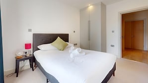 A hotel room with a bed, a bedside table with a lamp, a wardrobe, and a door leading to another room. - Bright 2BR Home w/ Private Garden Near Wimbledon (London)
