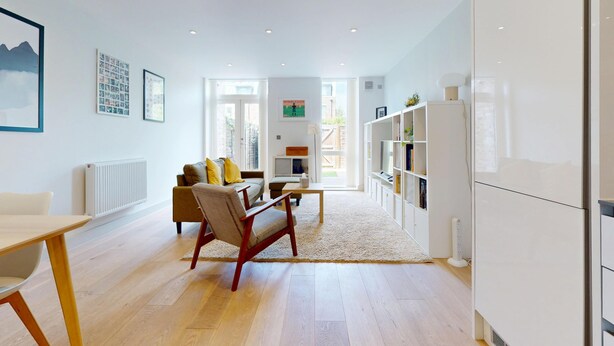 A modern living room with a sofa, coffee table, and a TV. There is a bookshelf and a radiator on the wall. - Bright 2BR Home w/ Private Garden Near Wimbledon (London)