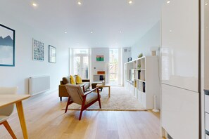Ein modernes Wohnzimmer mit einer Couch, einem Couchtisch und einem Fernseher. An der Wand befinden sich ein Bücherregal und eine Heizung.