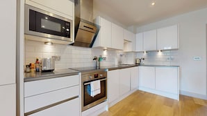 A modern kitchen with white cabinets, stainless steel appliances, and wooden flooring. - Bright 2BR Home w/ Private Garden Near Wimbledon (London)