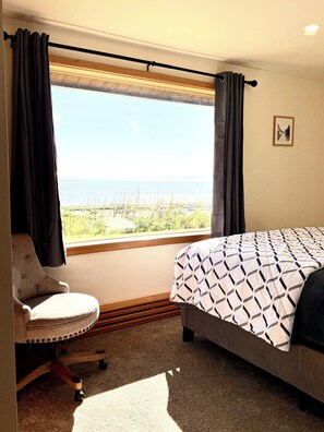 A bedroom with a bed, a chair, a window with curtains, and a view of the outdoors.