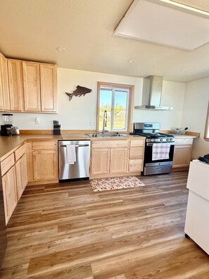 A kitchen with wooden cabinets, stainless steel appliances, a window with a view, and a wooden floor.