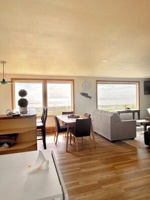 A spacious living area with a dining table, sofa, and large windows offering a view of the sea.