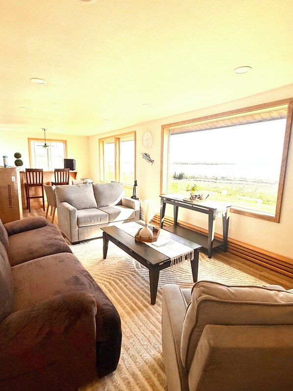 A living room with a sofa, armchairs, a coffee table, and a view through large windows.