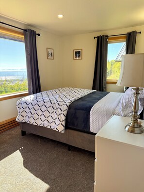 Un dormitorio con una cama, una mesita de noche, una lámpara, una ventana con cortinas y vistas al exterior.