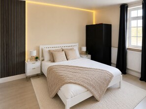 Ein Schlafzimmer mit einem Bett, Nachttischen, einem Kleiderschrank und einem Fenster mit Vorhängen.