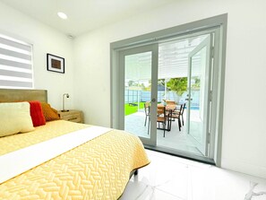 A bedroom with a bed, bedside table, and a view of an outdoor patio with a table and chairs. - Private Pool, Arcade Games & Family Fun Near Beach (Fort Lauderdale)