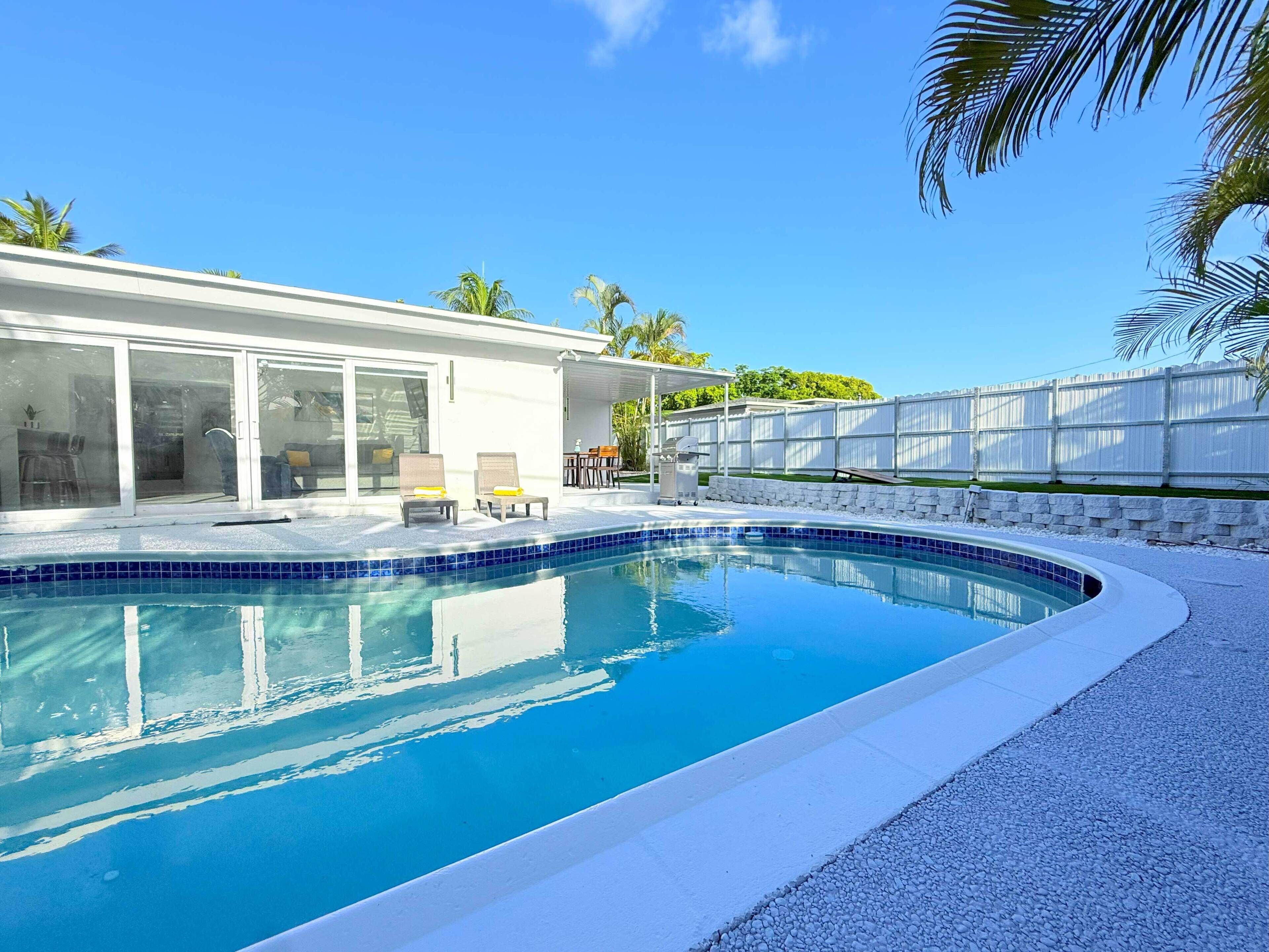 A modern pool area with a clear blue pool, a covered patio, and a white fence.