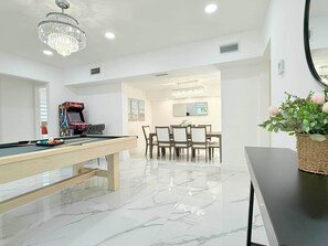 A modern living room with a pool table, a dining area with a chandelier, and a mirror on the wall. - Private Pool, Arcade Games & Family Fun Near Beach (Fort Lauderdale)