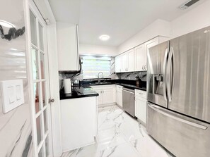 A modern kitchen with white cabinets, a black countertop, and stainless steel appliances. - Private Pool, Arcade Games & Family Fun Near Beach (Fort Lauderdale)