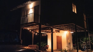Una casa de dos pisos con balcón, un porche cubierto y guirnaldas de luces.