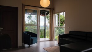 A room with a sliding glass door leading to a balcony, a dark blue armchair, a black sofa, and a hanging light fixture.