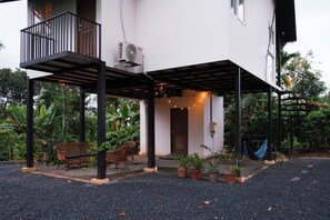 Ein zweistöckiges Gebäude mit überdachter Terrasse, Sitzgelegenheiten im Freien und Blumentöpfen.