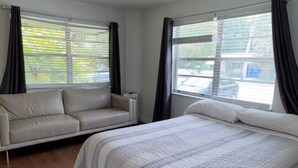 Une chambre à coucher comprenant un lit, un canapé, un ventilateur de plafond et de grandes fenêtres avec des rideaux.