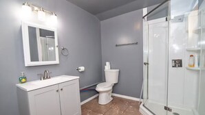 Casa de banho com uma sanita, uma pia branca e um chuveiro com divisória de vidro, e um espelho iluminado.