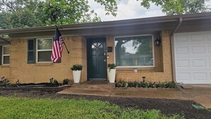 A two-story house with a brick exterior, a front door, a garage, and an American flag. - A World Cup Cottage in FarmersBranch (Farmers Branch)