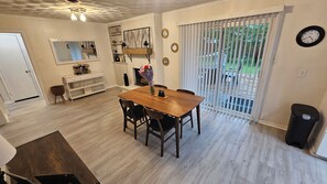 Un coin repas avec une table et des chaises en bois, une cheminée, un miroir et une vue à travers une porte-fenêtre coulissante.