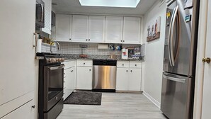 A modern kitchen with white cabinets, a stainless steel dishwasher, a built-in oven, a refrigerator, and a skylight. - A World Cup Cottage in FarmersBranch (Farmers Branch)