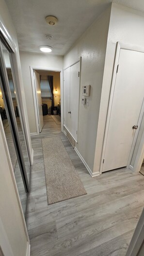 Un couloir avec un plancher en bois, un tapis, une porte avec une serrure et un thermostat fixé au mur.