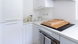 A modern kitchen with white cabinetry, a black induction cooktop, and a wooden cutting board.