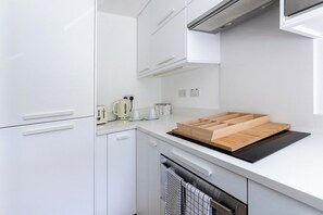 Een moderne keuken met witte kastjes, een zwarte inductiekookplaat en een houten snijplank.