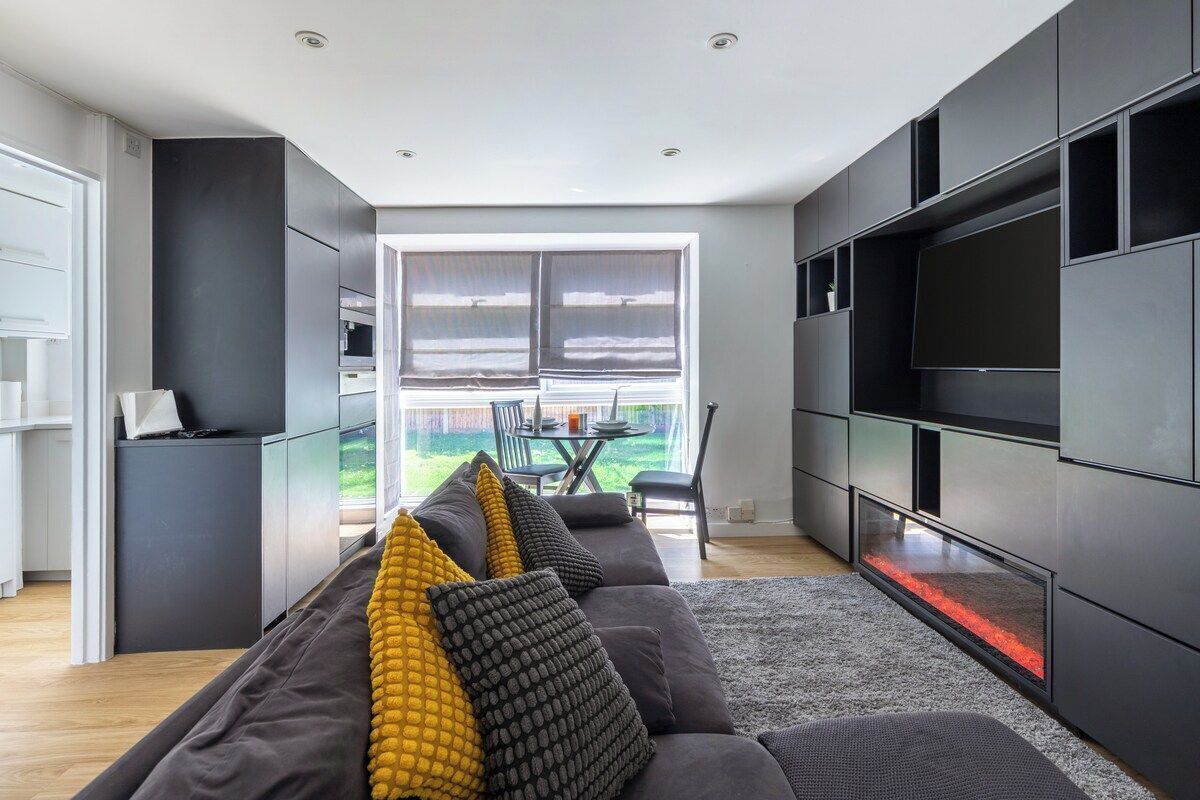 A modern living room with a dark-colored sofa, a flat-screen TV mounted on the wall, and a glass fireplace.