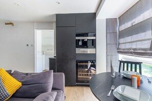 A modern kitchen with built-in appliances, a dining area with a round table, and a sofa with cushions. - Modern 2-Bed | 5 Mins to Ealing Broadway Station (London)