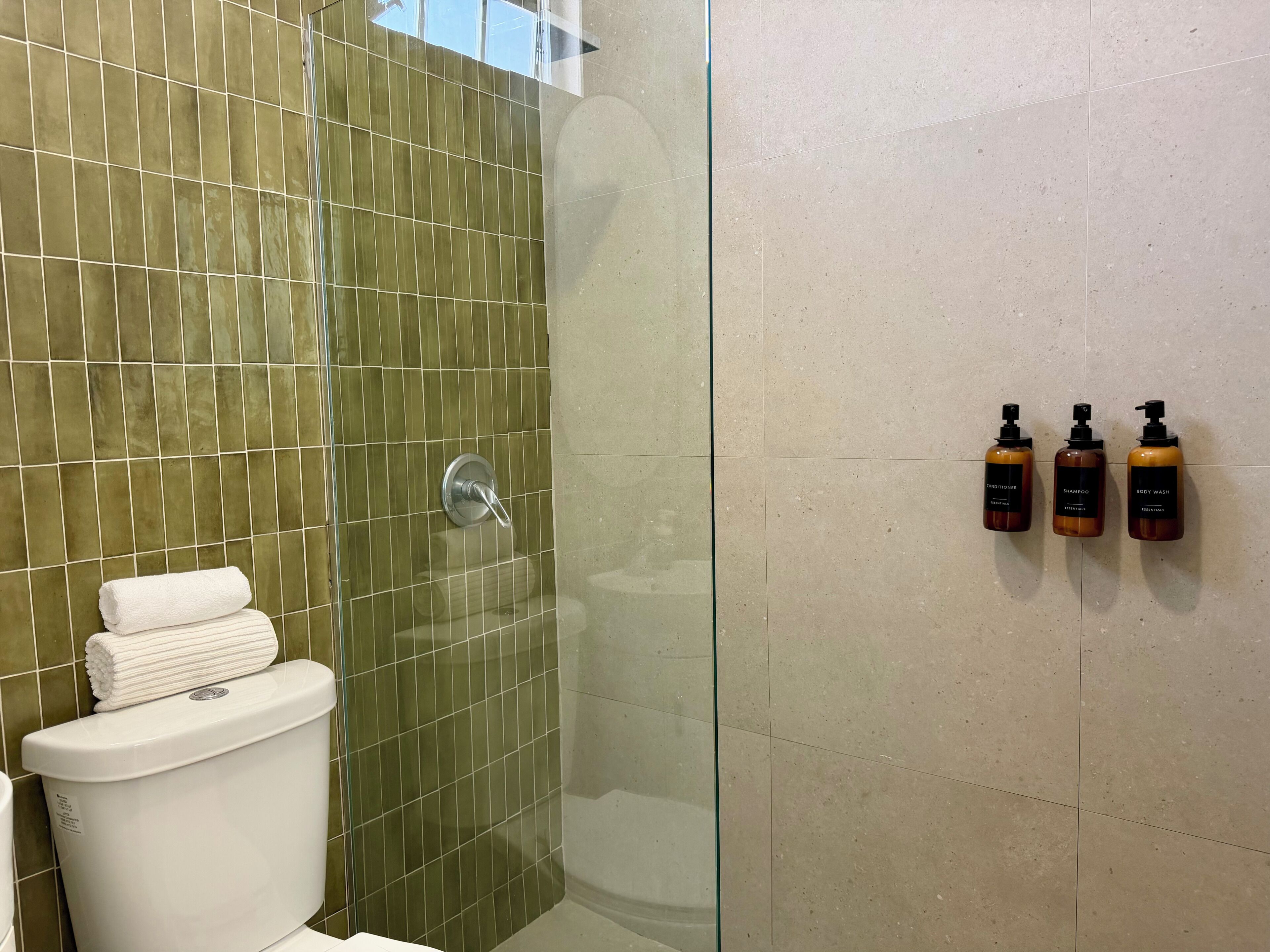 Ein Badezimmer mit Duschkabine aus Glas, Toilette und drei Pflegeprodukten an der Wand.