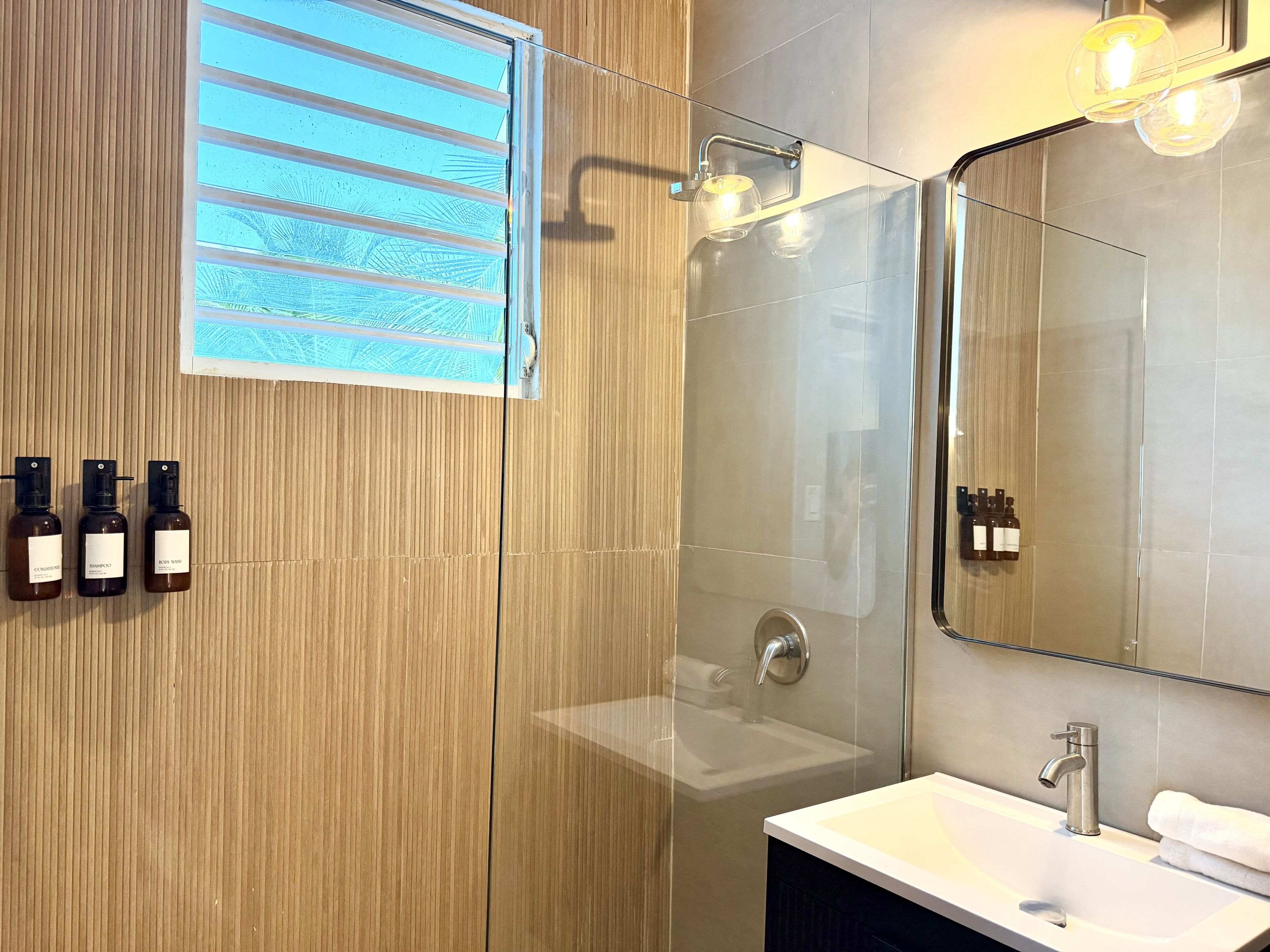 Un baño moderno con cabina de ducha de vidrio, un espejo grande y un lavabo.