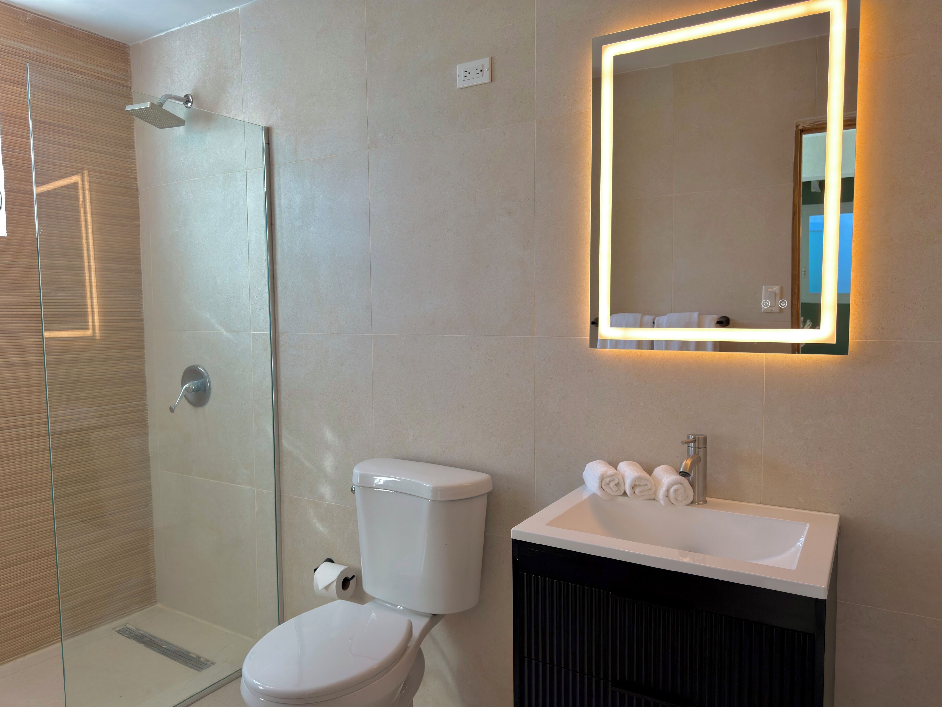 A modern bathroom with a glass-enclosed shower, a toilet, a sink with a mirror, and a towel rack.