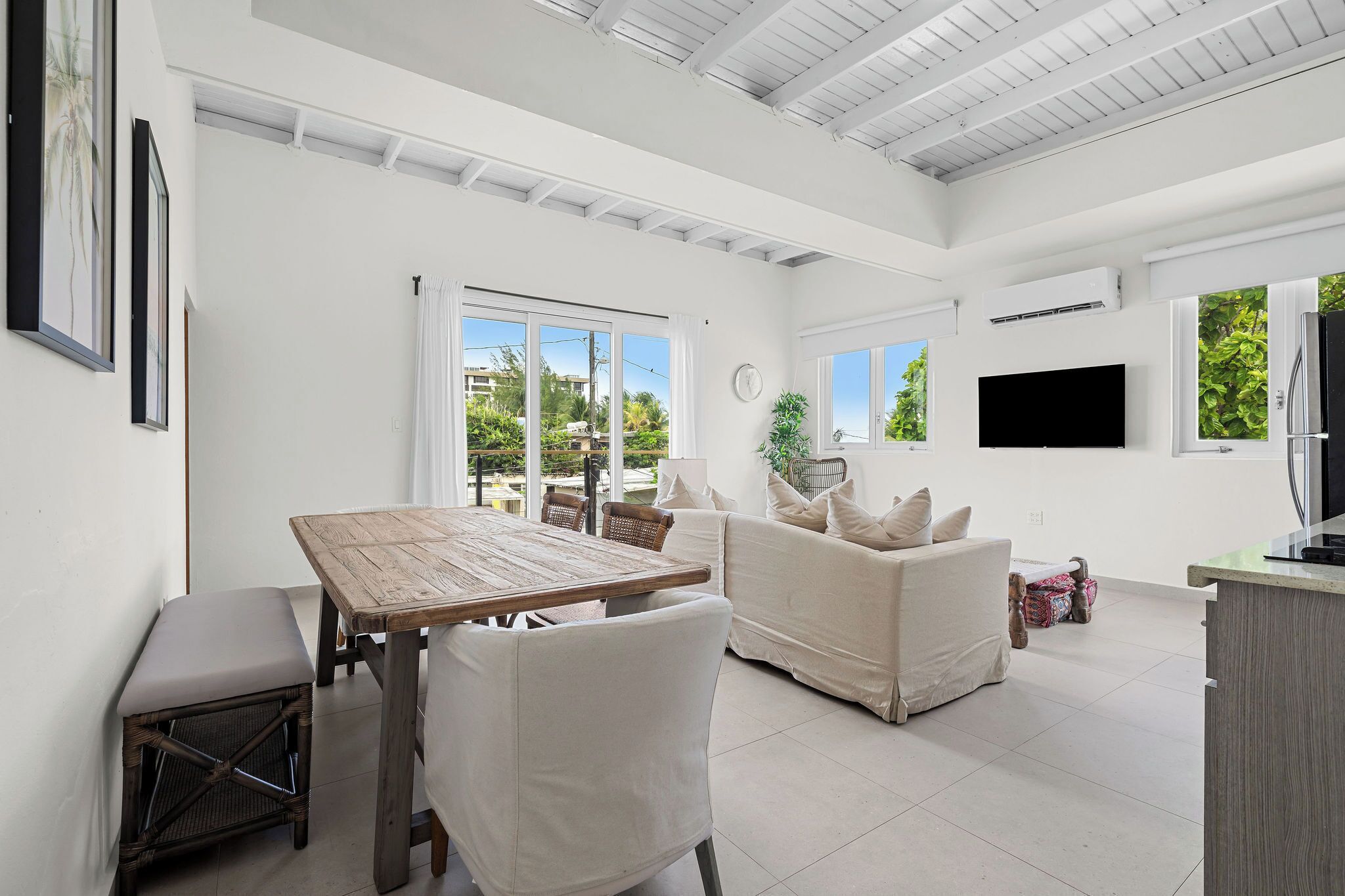 A spacious living area with a wooden table and chairs, a sofa, and a television mounted on the wall.