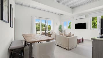 A spacious living area with a wooden table and chairs, a sofa, and a television mounted on the wall.