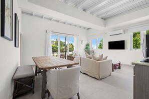 A spacious living area with a wooden table and chairs, a sofa, and a television mounted on the wall.