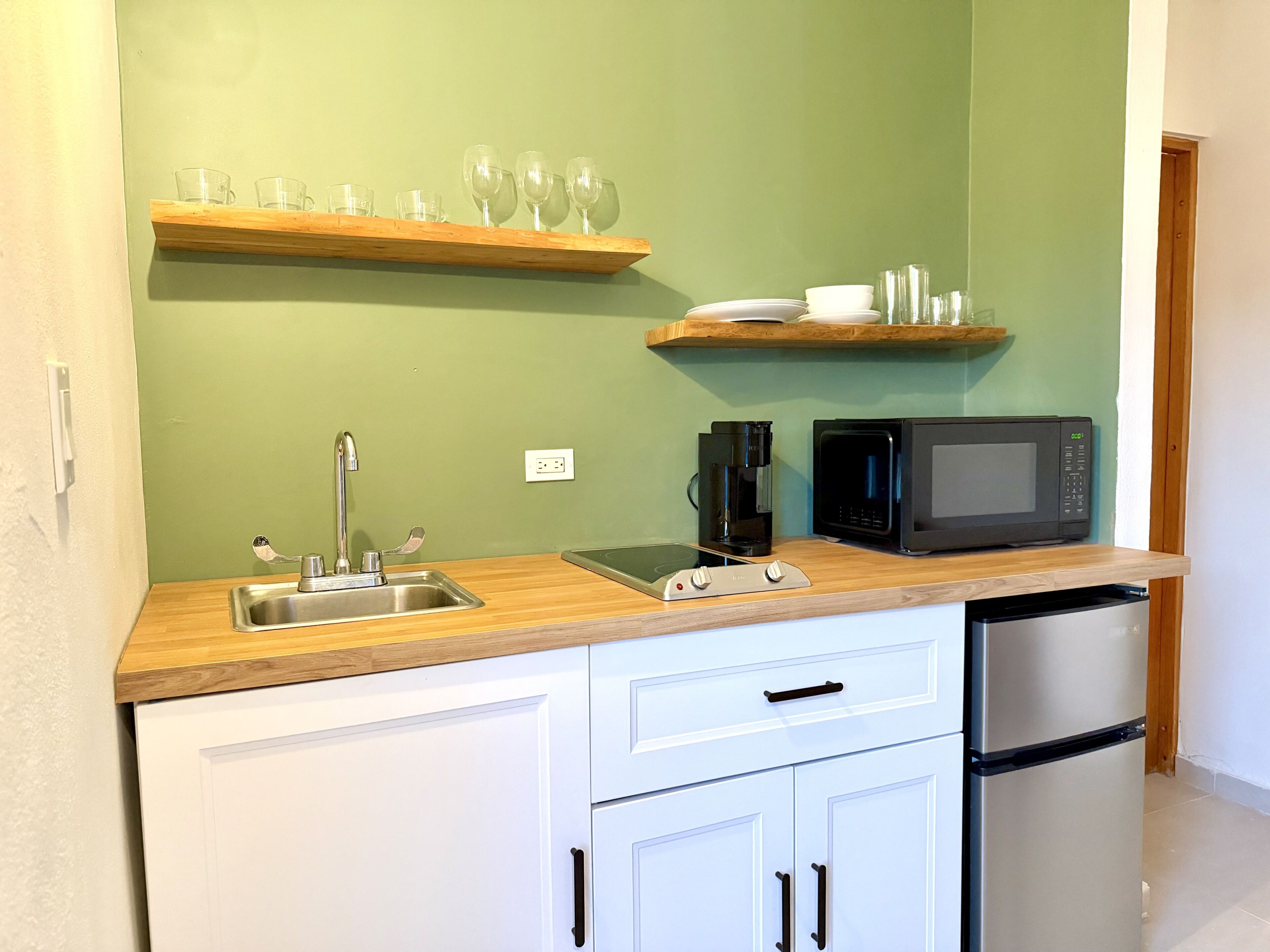 A compact kitchen with a sink, coffee maker, microwave, and a refrigerator.