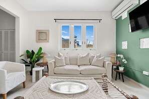 A living room with a sofa, a coffee table, a plant, and a window with a view.