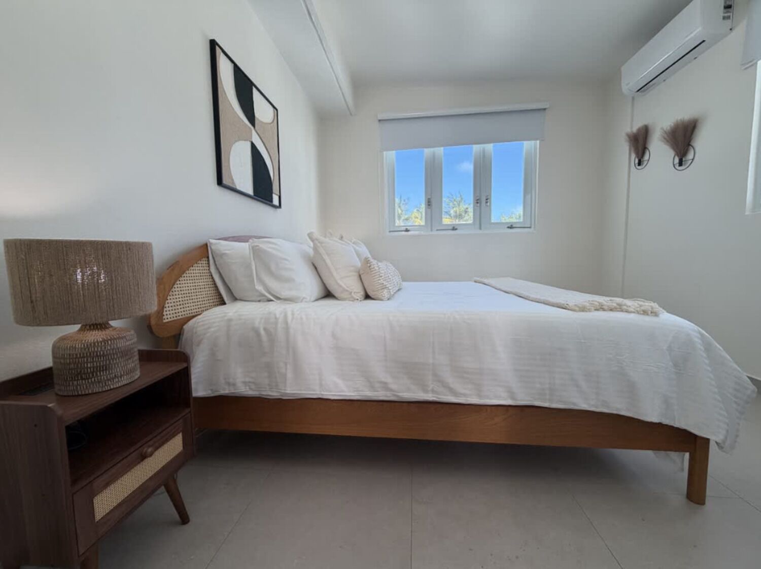 A bedroom with a bed, bedside table, lamp, and a window.