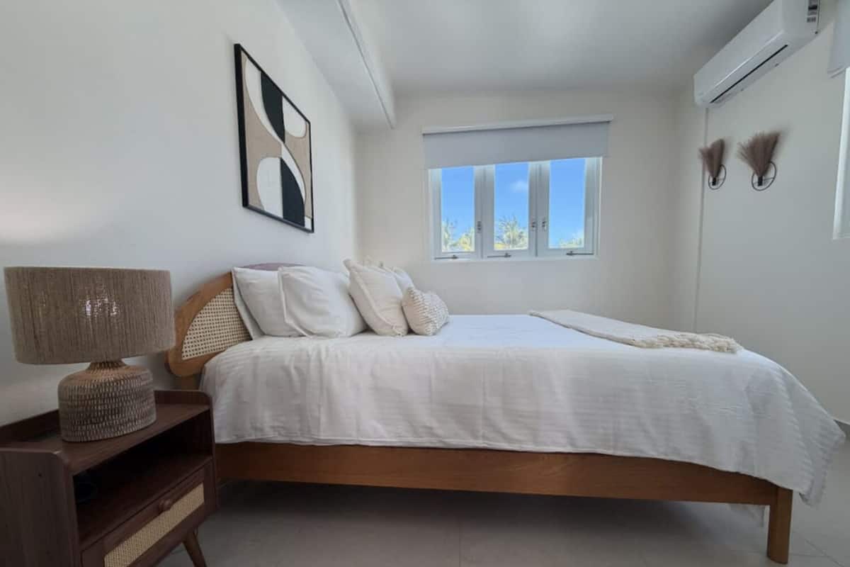 A bedroom with a bed, bedside table, lamp, and a window.