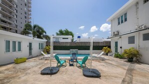 A rooftop pool area with lounge chairs, a table, and potted plants.