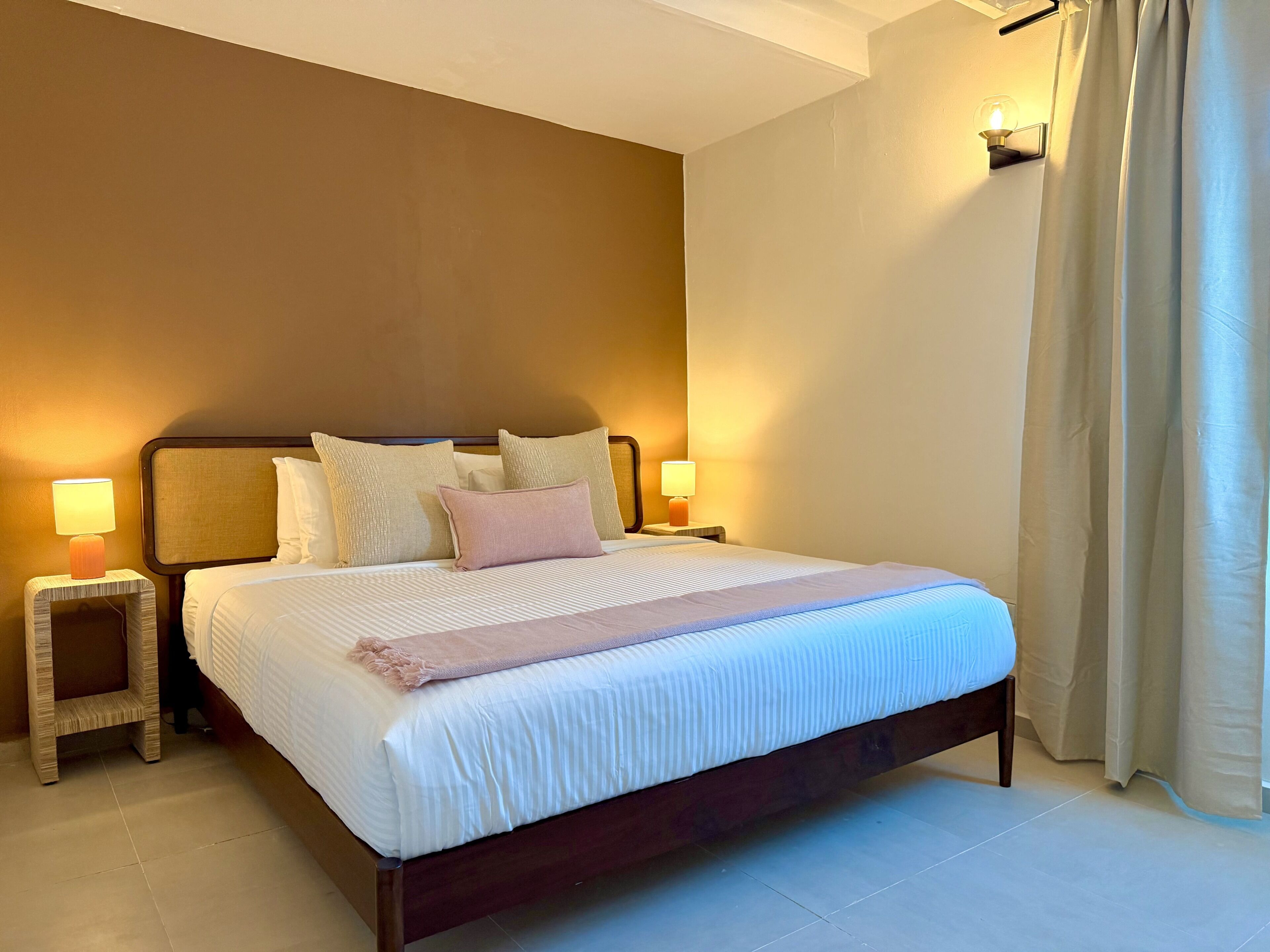 A neatly made bed with pillows, a bedside lamp, and a wall-mounted light fixture.