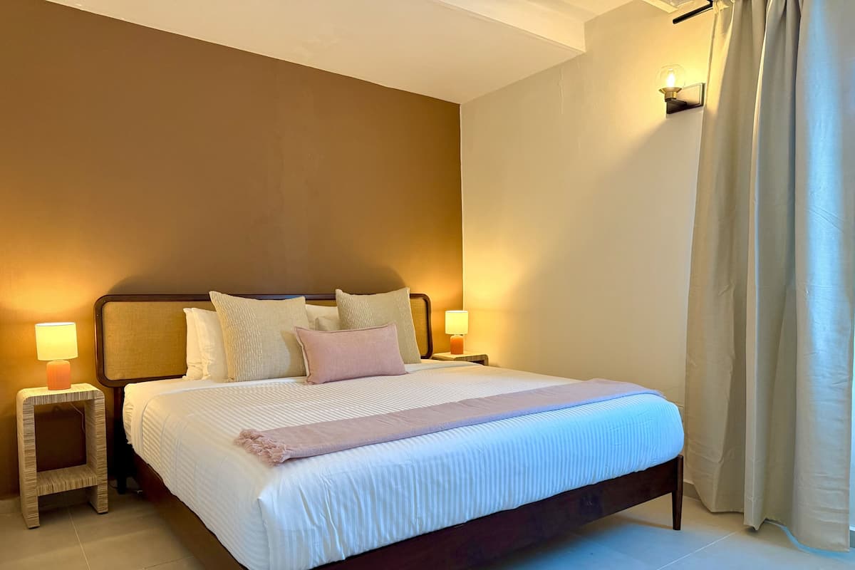 Una cama bien hecha con almohadas, una lámpara de noche y un aplique de pared.