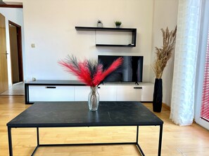 Un saló modern amb una taula de cafè negra, un televisor de pantalla plana, armaris blancs i plantes decoratives.