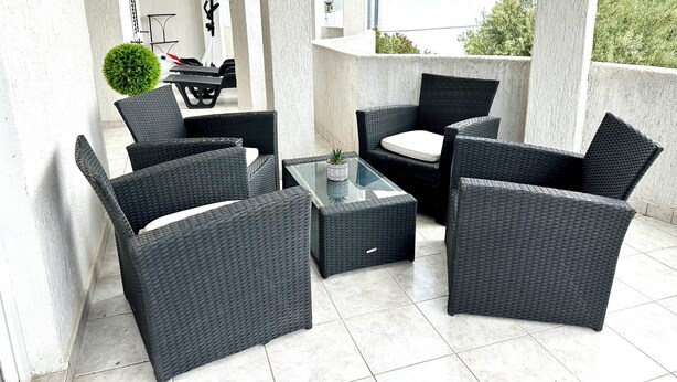 A balcony with wicker furniture, a glass table, and a potted plant. - Magic Sunset – apartman za 4 osobe s velikim balkonom i orbitrekom (Pirovac)
