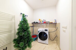 A laundry room with a washing machine, a small Christmas tree, and a shelf with cleaning supplies. - Luxury Aparthotel MejtasHills - Old Town (Sarajevo)