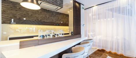 Un espace bar moderne avec un comptoir blanc, des tabourets de bar en cuir, un mur à motifs zébrés et un grand luminaire suspendu.