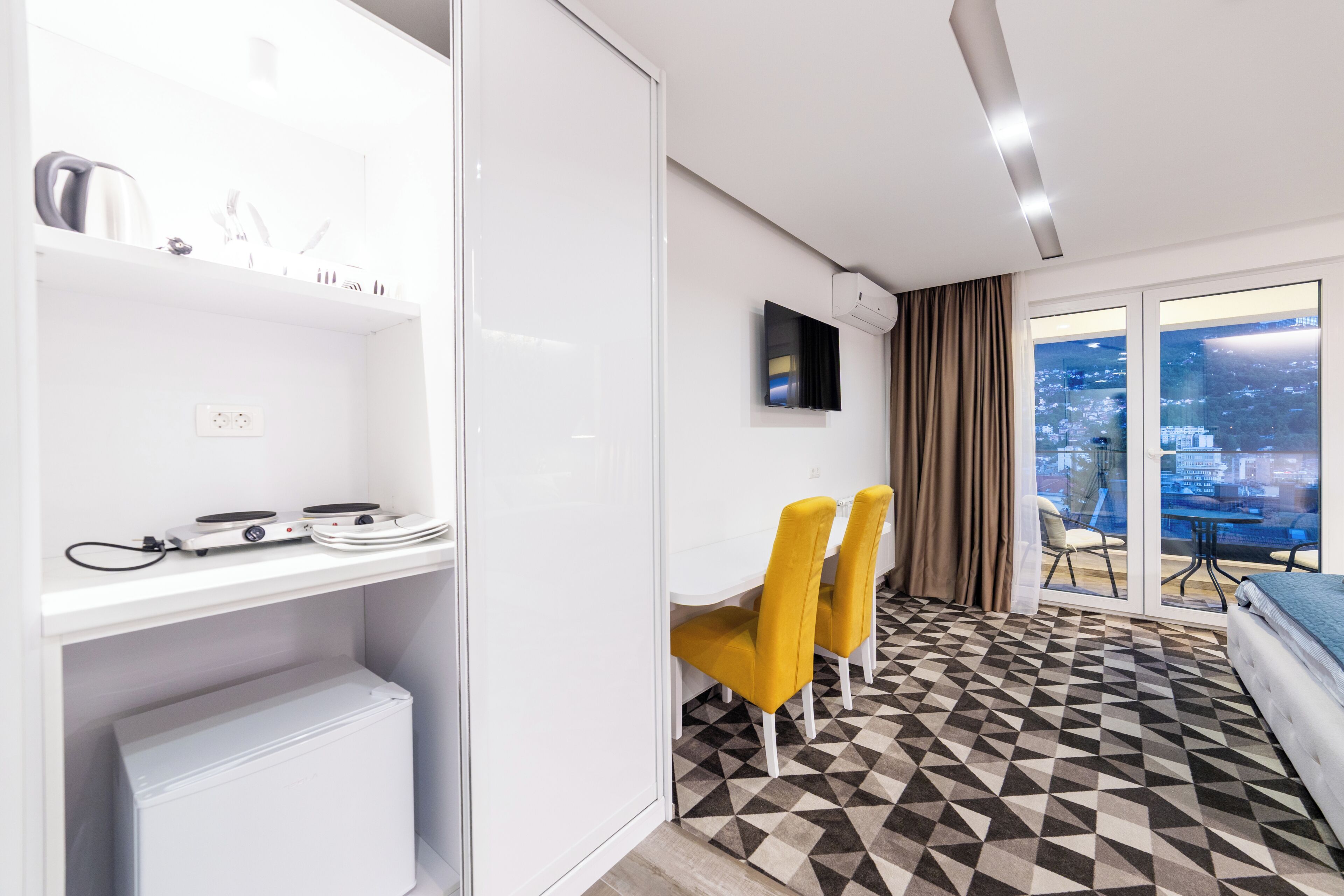 A hotel room with a dining area, a bed, a TV, and a city view.
