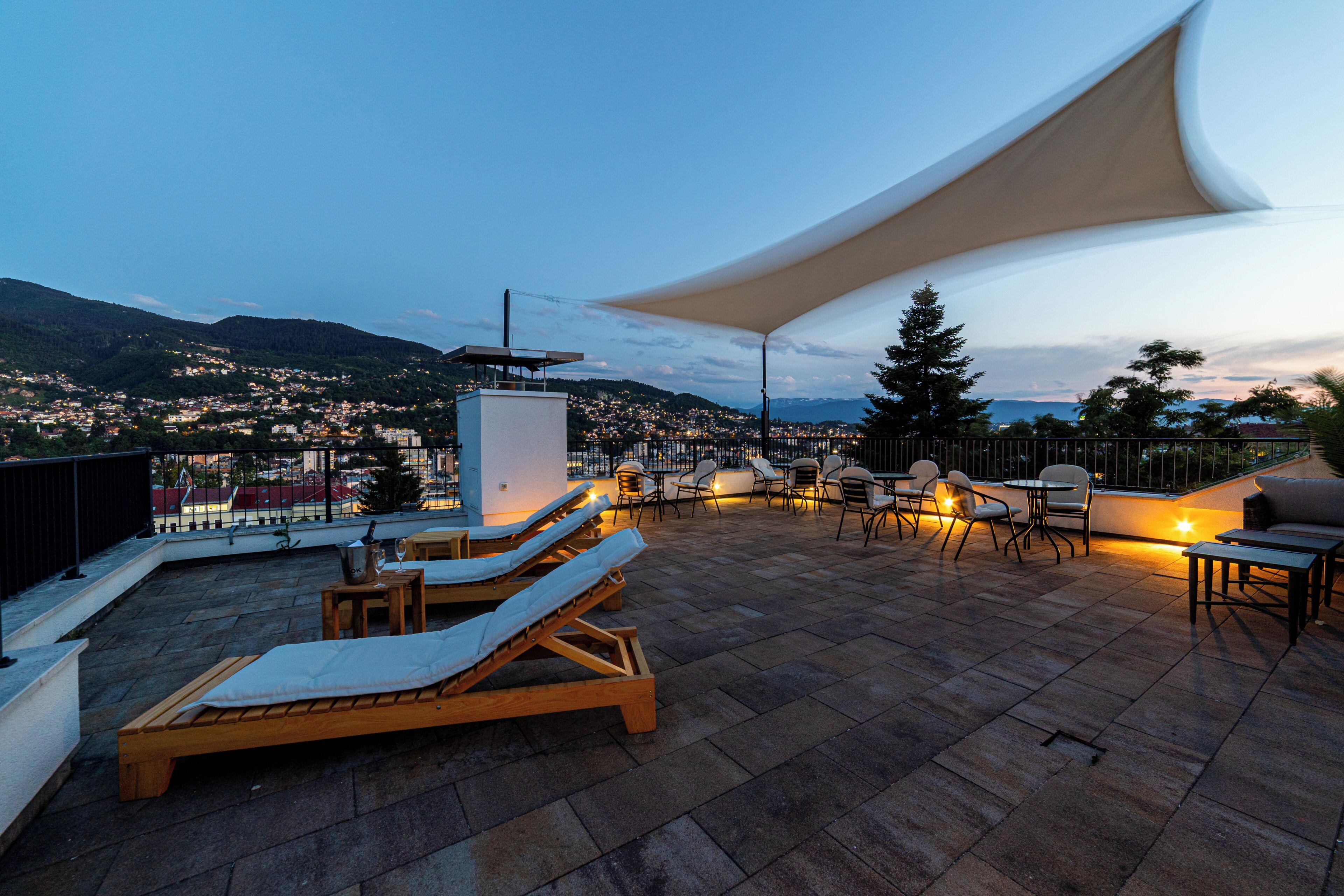 A rooftop terrace with lounge chairs, a table, and a large umbrella providing shade.