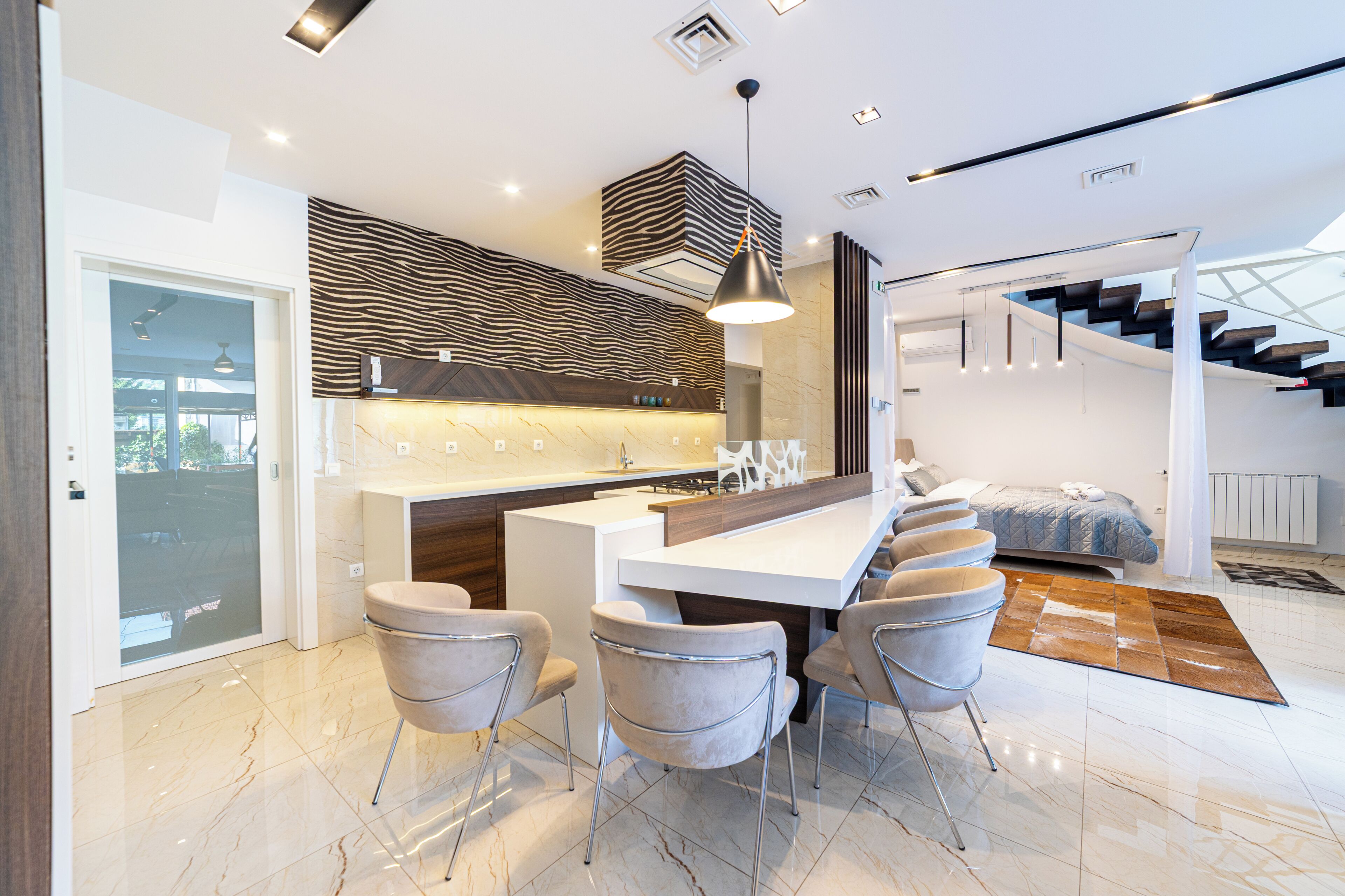 A modern kitchen with a central island, bar stools, and a staircase leading to an upper level.