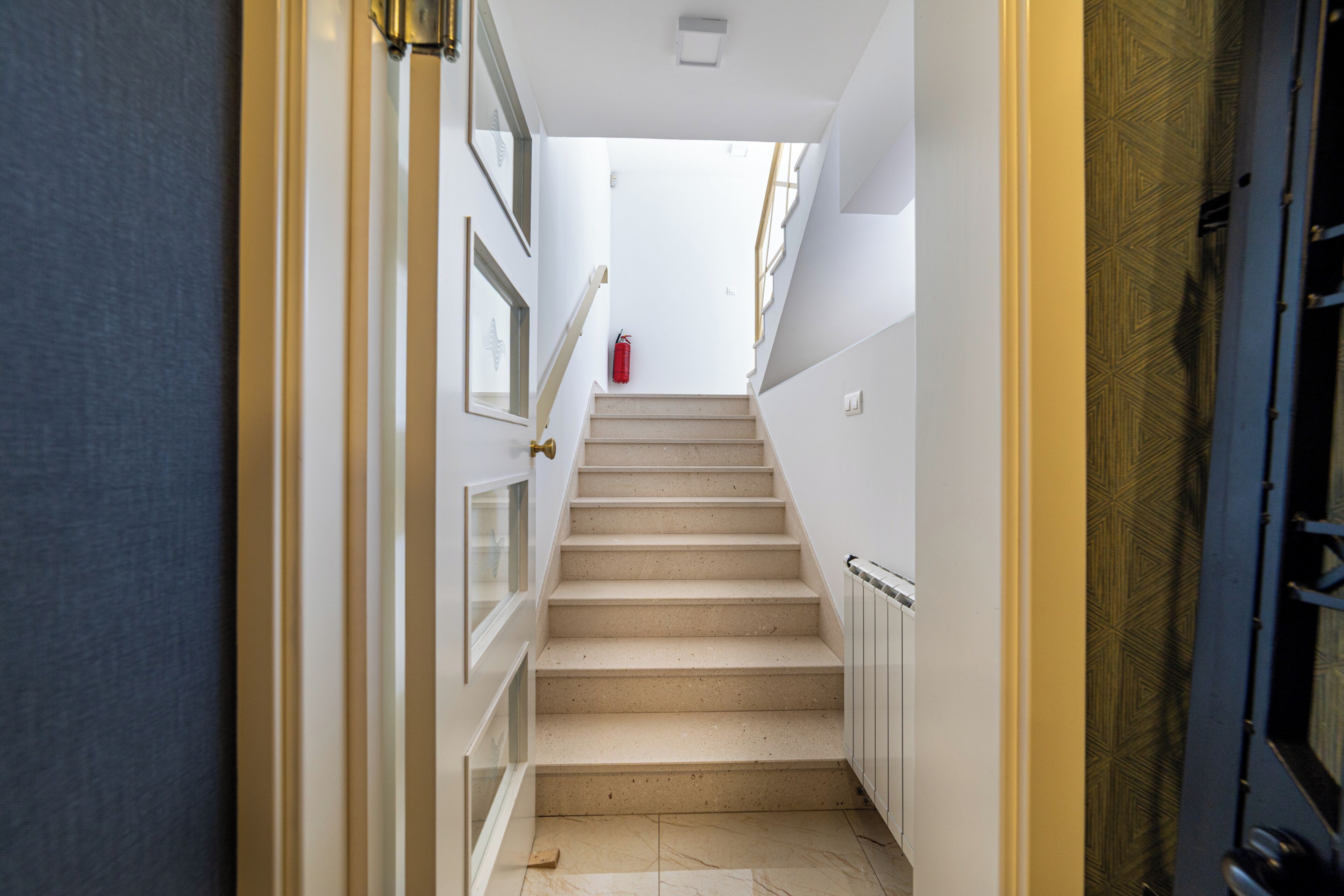 A staircase with a handrail, a fire extinguisher, and a door with a geometric pattern.