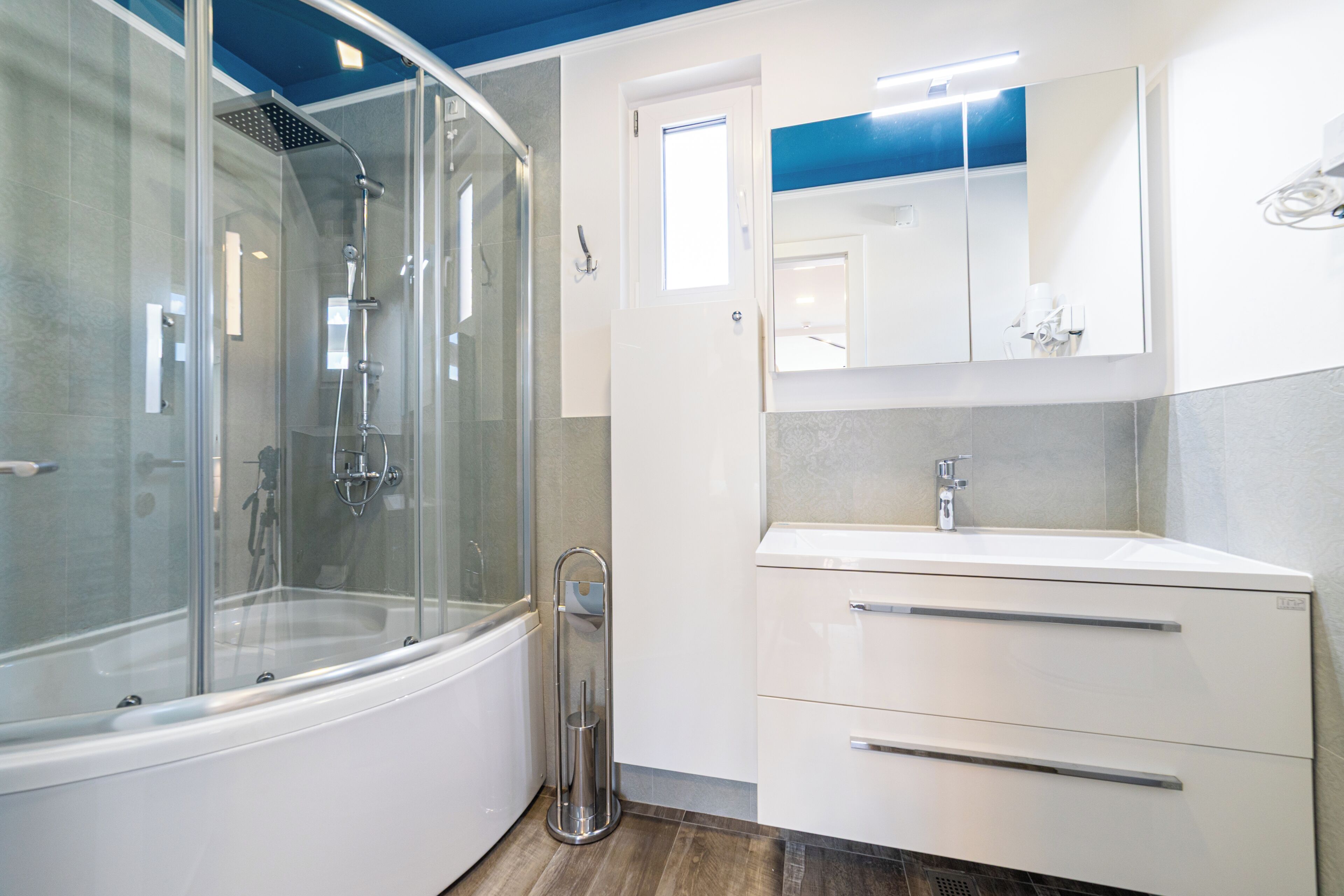 A modern bathroom with a glass-enclosed shower, a white vanity with a mirror, and a door leading to another room.