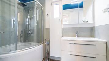 A modern bathroom with a glass-enclosed shower, a white vanity with a mirror, and a door leading to another room.